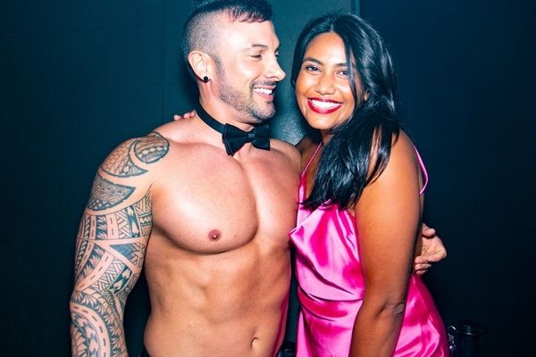 A hen in pink satin smiling with a topless waiter in a bow tie