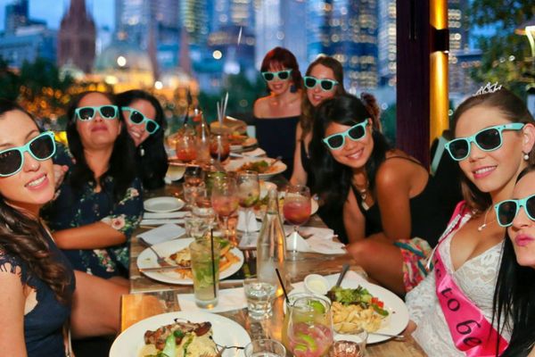 Hens in matching sunglasses at a long dinner table with the city skyline behind