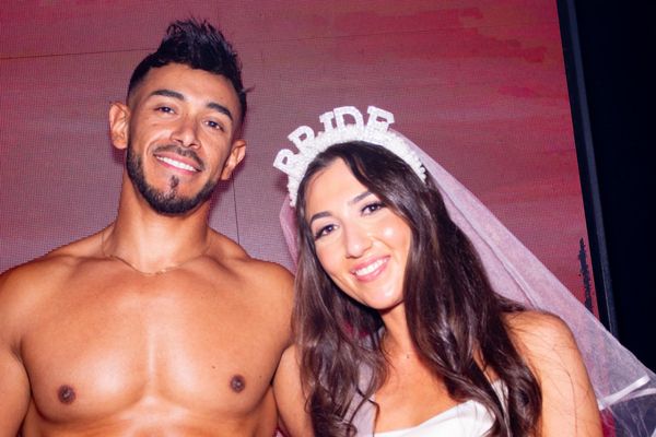 A bride to be in a veil and tiara smiling beside a shirtless waiter
