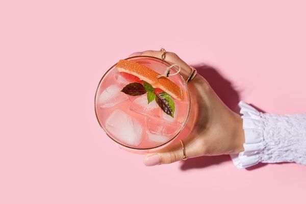 A hand holding a pink grapefruit cocktail against a pink background