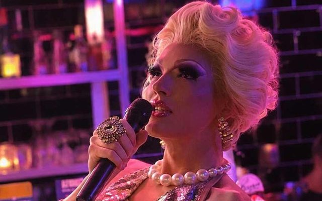A drag performer in sequins and pearls singing into a microphone