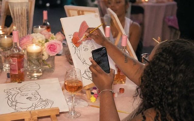 A life drawing table with wine glasses, candles and finished sketches, a hen photographing her drawing
