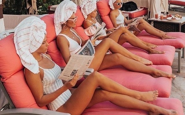 Friends in towel turbans relaxing on pink poolside daybeds at a day spa