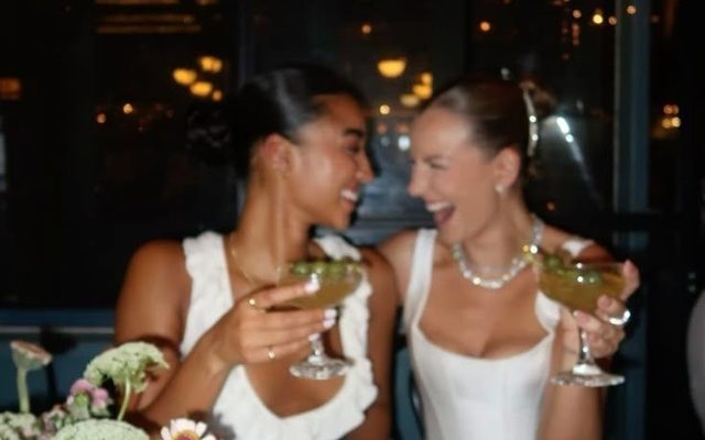 Two friends in white clinking cocktails across a restaurant table