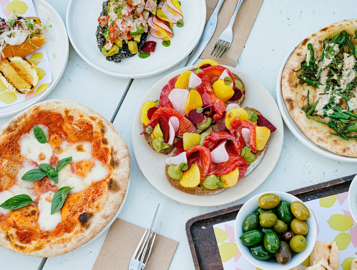 A brunch table spread with pizzas, salmon and beetroot on toast, olives and lemons