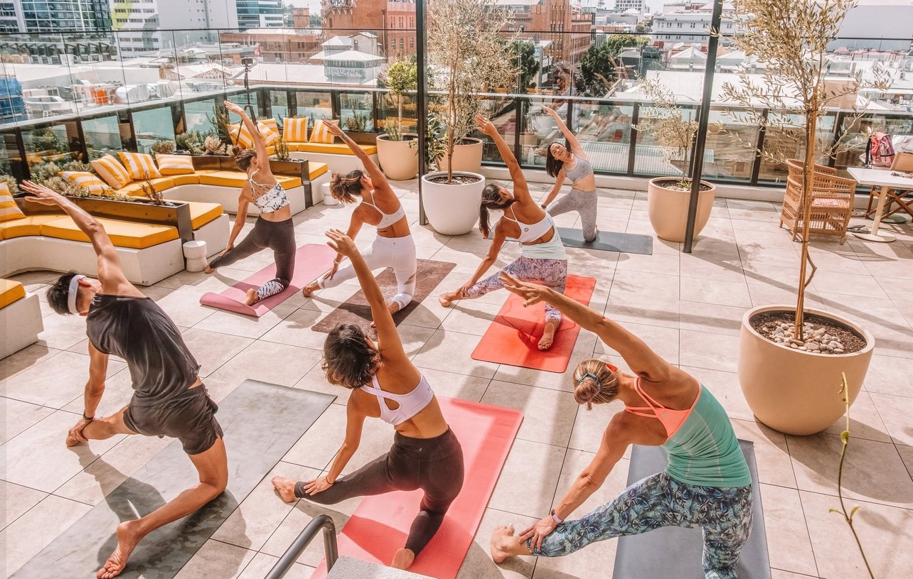 A hens yoga class stretching on bright mats on a sunny city rooftop