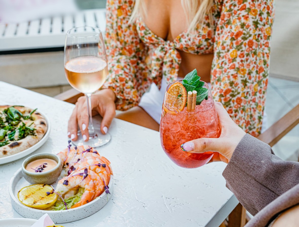 A glass of rose and a spritz with an orange slice and mint on a brunch table with prawns and pizza