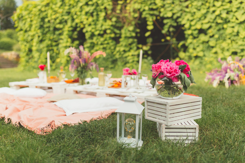 A picnic set up on the lawn with white crates, lanterns, cushions and pink flowers