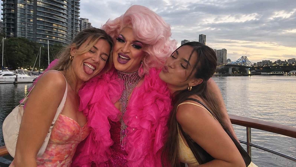 Our drag queen in a pink feather boa squeezed between two hens on a boat on the river at sunset