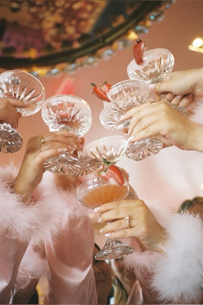 Hands clinking coupe cocktails trimmed with white feathers