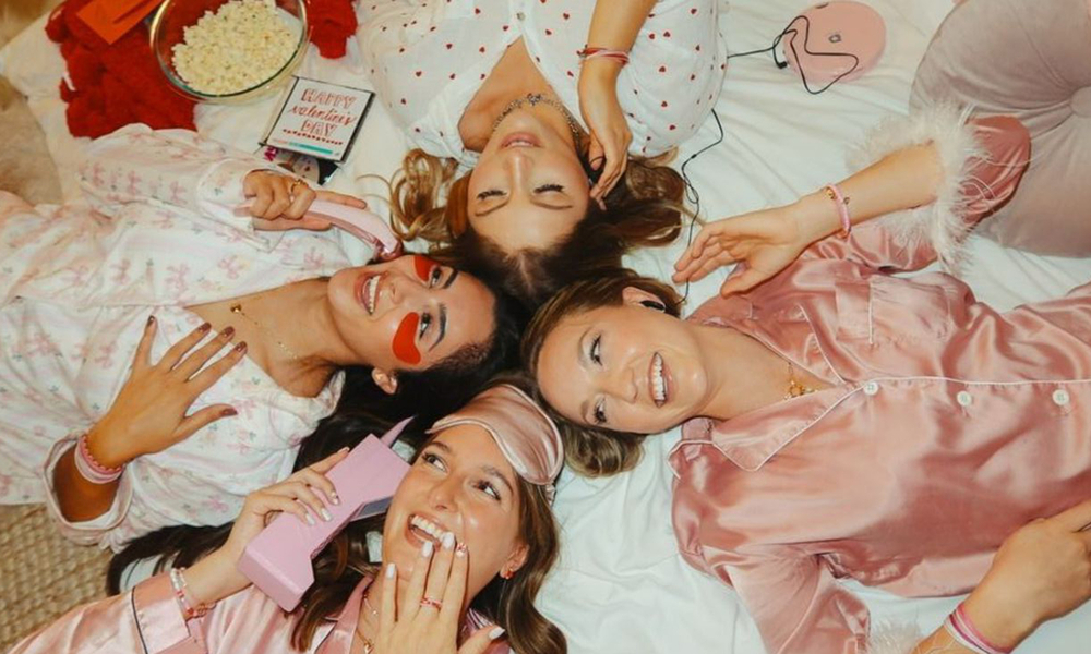 Friends in satin pyjamas lying in a circle with their heads together, seen from above