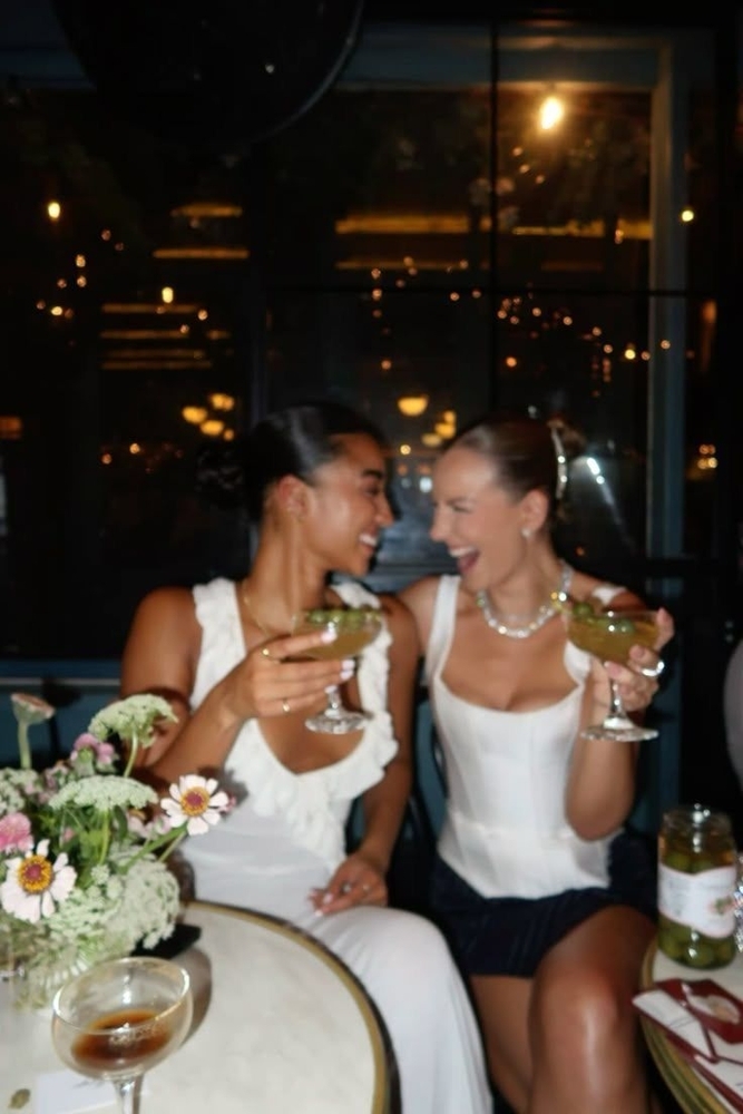 Two women in white toasting cocktails at a night bar