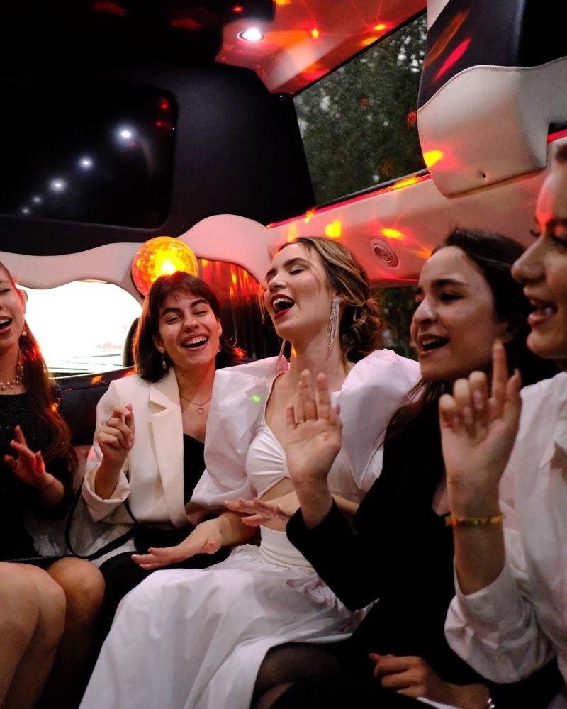 Three friends laughing and singing together in the back of a party bus