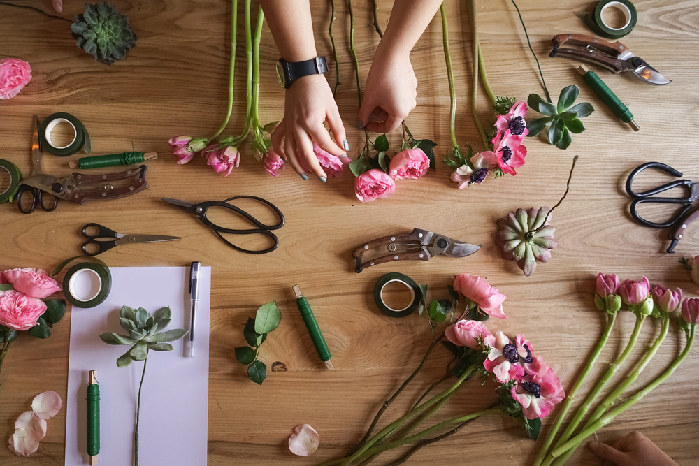 Hands arranging pink flowers on a wooden table