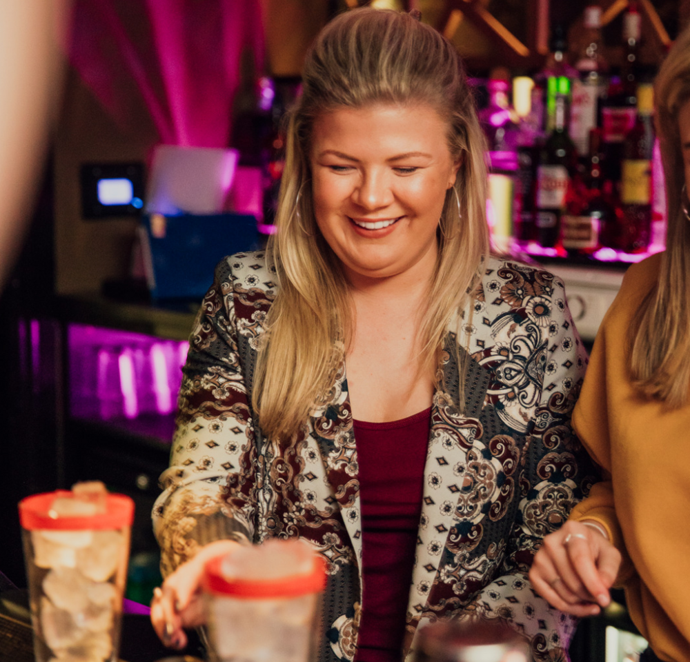 A hen laughing as she shakes a cocktail behind the bar