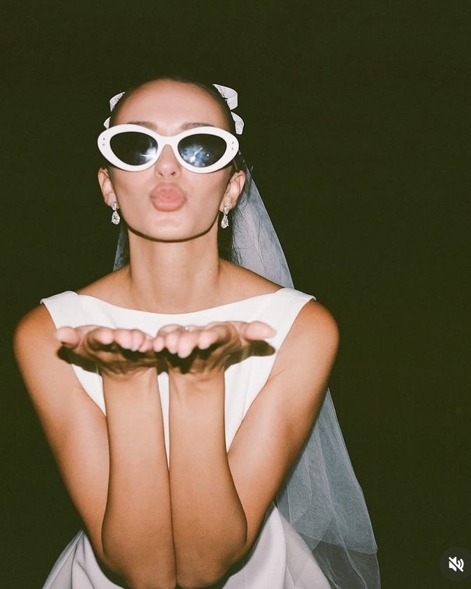 The bride in her veil and white heart sunglasses blowing a kiss to the camera