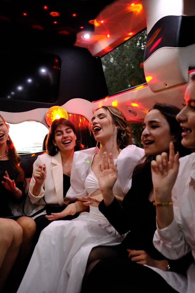 Friends laughing and singing along in the back of a limo under the party lights
