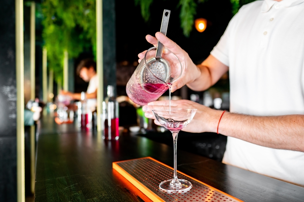 A bartender strains a pink cocktail into a glass at a hens class