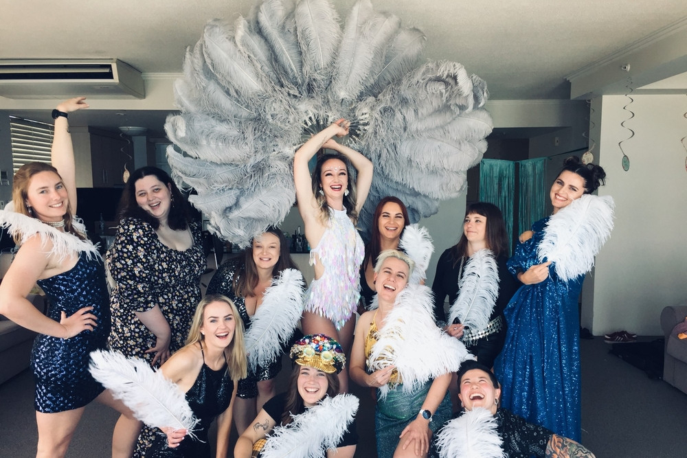 A hens crew posing with big white and grey feather fans at their burlesque class