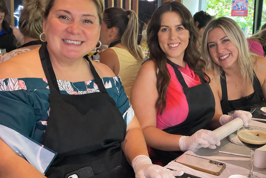 Three smiling friends in aprons rolling out clay at a workshop table
