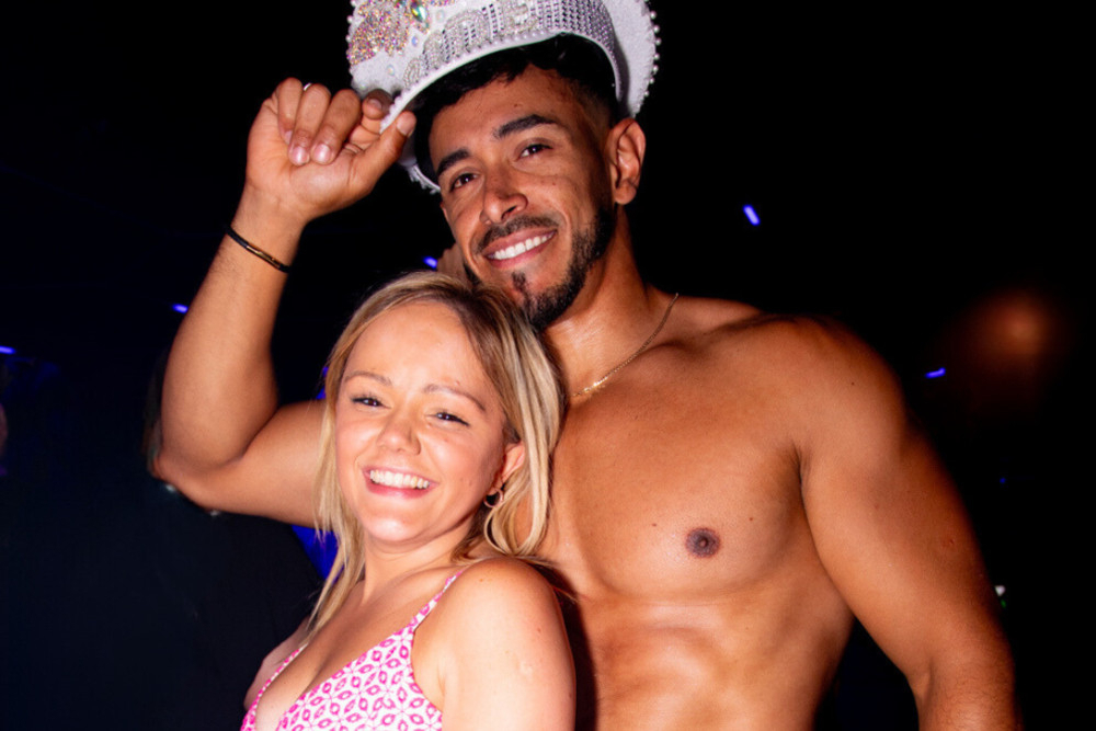 A laughing hen in pink beside our topless waiter, who is wearing her sparkly Bride cap