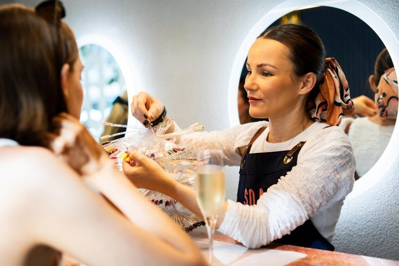 A nail artist holds up colour swatches for a hen, a glass of bubbly beside her