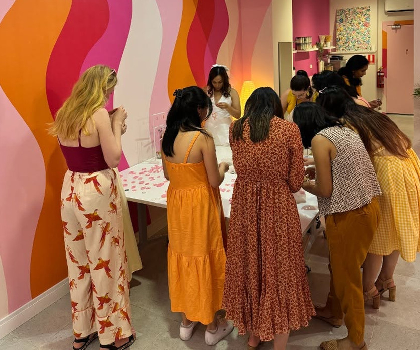 A hens group gathered round a table in a bright pink and orange studio