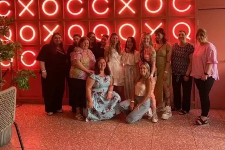 A hens crew dressed for dinner, posing in front of a wall of glowing red neon letters