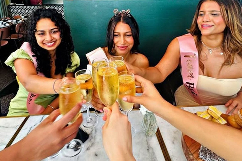 Hens in sashes and a tiara clink glasses of bubbles across a marble table