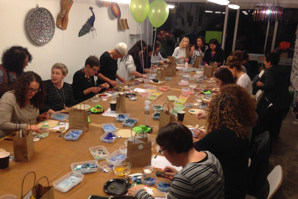Guests work on glass jewellery designs along a long studio table with balloons overhead