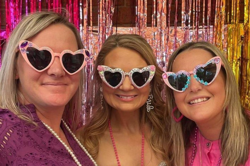 Three friends in pink heart sunglasses posing in front of pink and gold tinsel