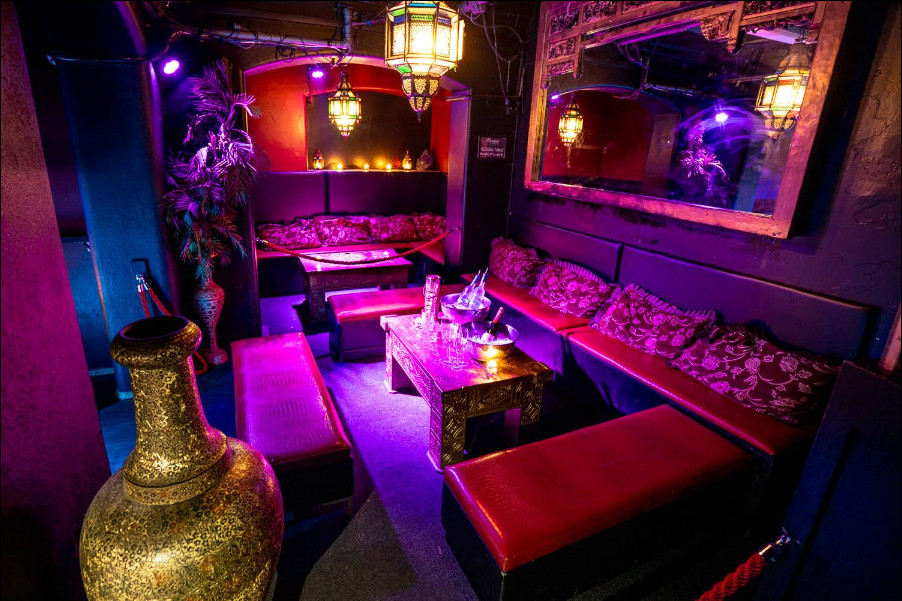 A private room with red velvet booths, Moroccan lanterns and a gold vase, lit pink and purple
