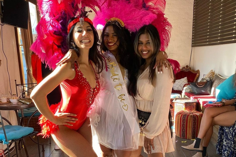 A bride with a burlesque dancer in a red costume and pink feather headdress
