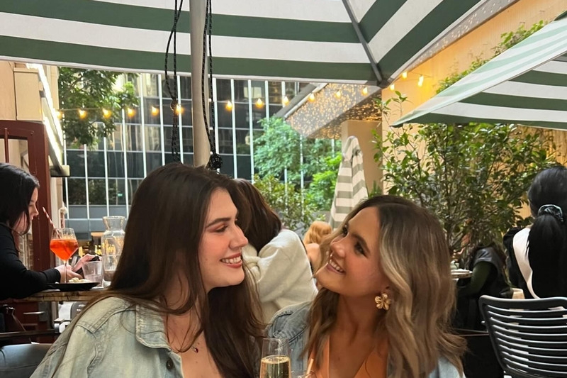 Two friends laughing over glasses of bubbly at an outdoor table