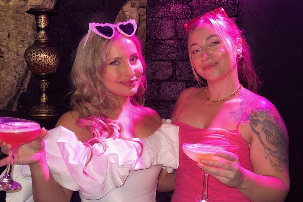 Two friends raising pink cocktails in a candlelit Moroccan-style lounge