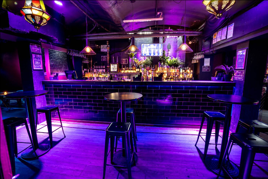 A purple-lit lounge bar with a tiled counter, bar stools and Moroccan lanterns