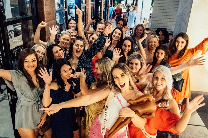 A big group of friends cheering with arms out at a riverside bar