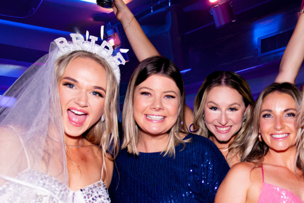 The bride in her veil and Bride headband laughing with her friends in sequins under a spotlight