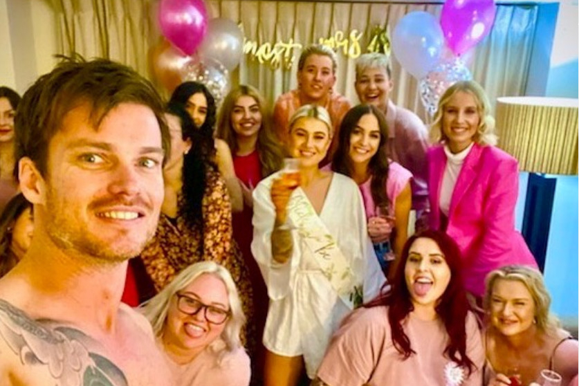 Our shirtless waiter taking a selfie with a smiling hens group and pink balloons