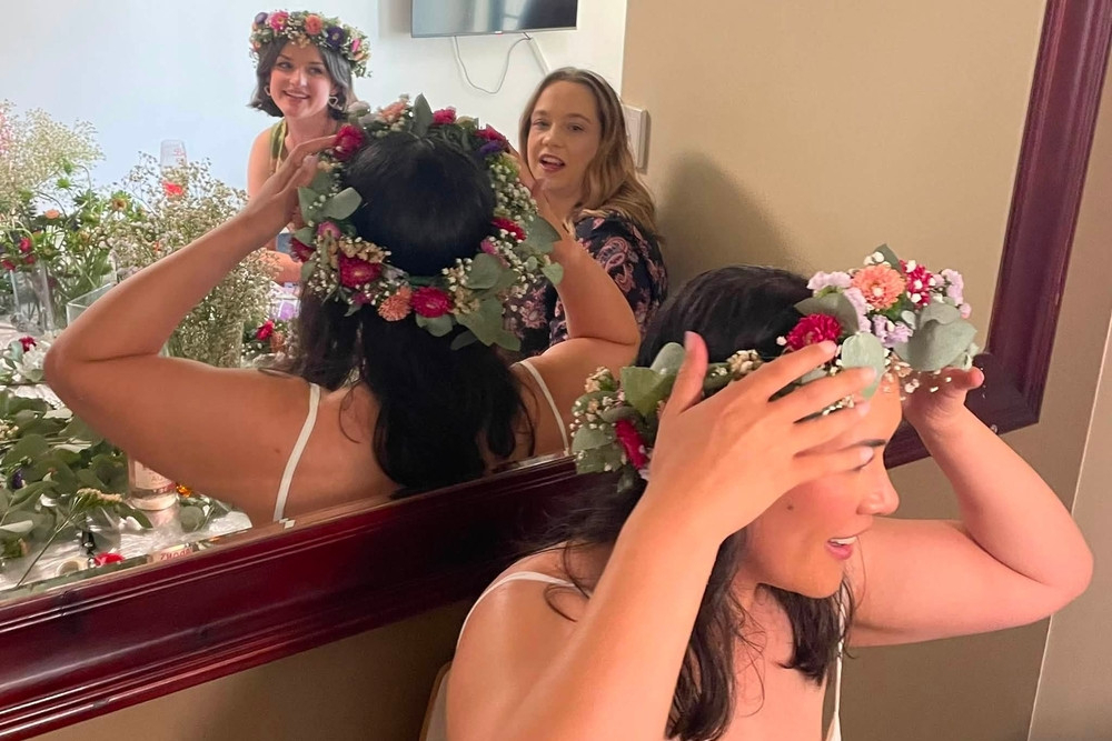 A guest placing a fresh flower crown on her head in front of a mirror