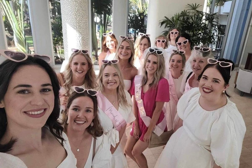 A big group of friends in white and pink squeezed into a sunny selfie