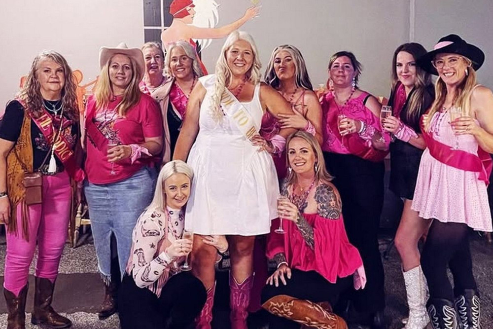 A big cowgirl hens crew in pink hats and boots around the bride in white