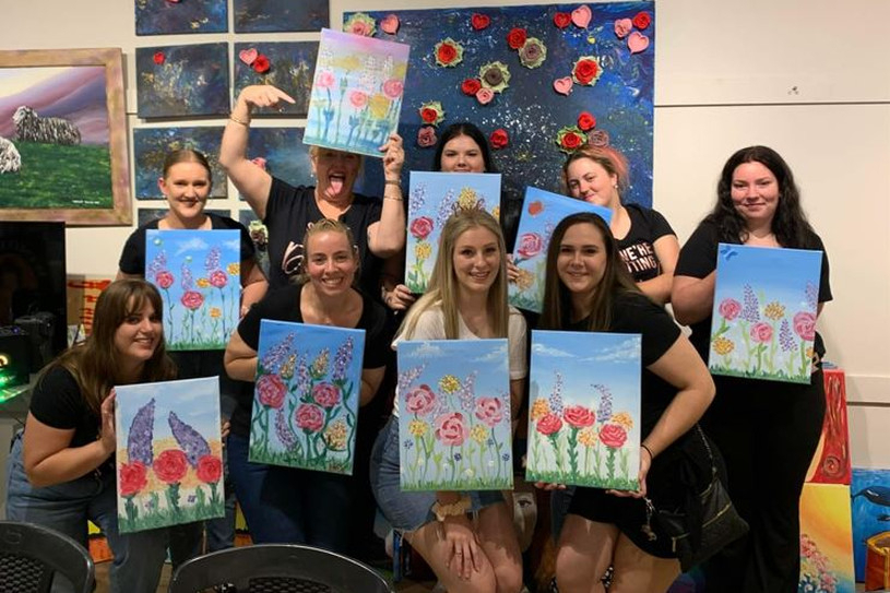 Friends holding up their finished floral paintings in an art studio