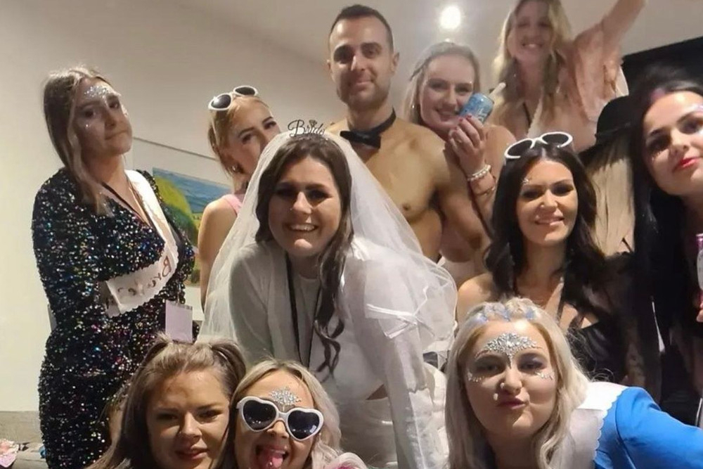 A hens crew squeezed into a selfie around the bride in her veil, our shirtless waiter grinning behind them
