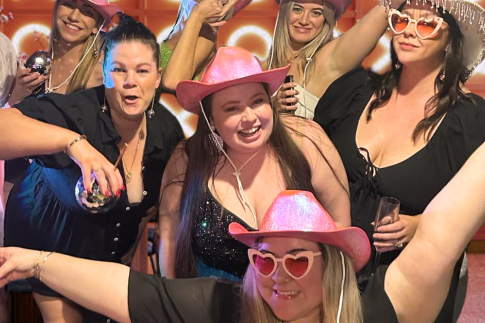 A hens crew in pink cowgirl hats and heart sunglasses cheering together