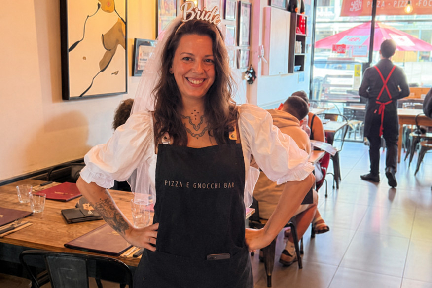 The bride in a Bride headband and apron smiling inside an Italian restaurant before a pizza class