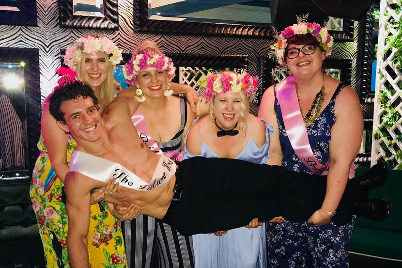 Hens in flower crowns and sashes laughing as they lift our topless waiter off his feet