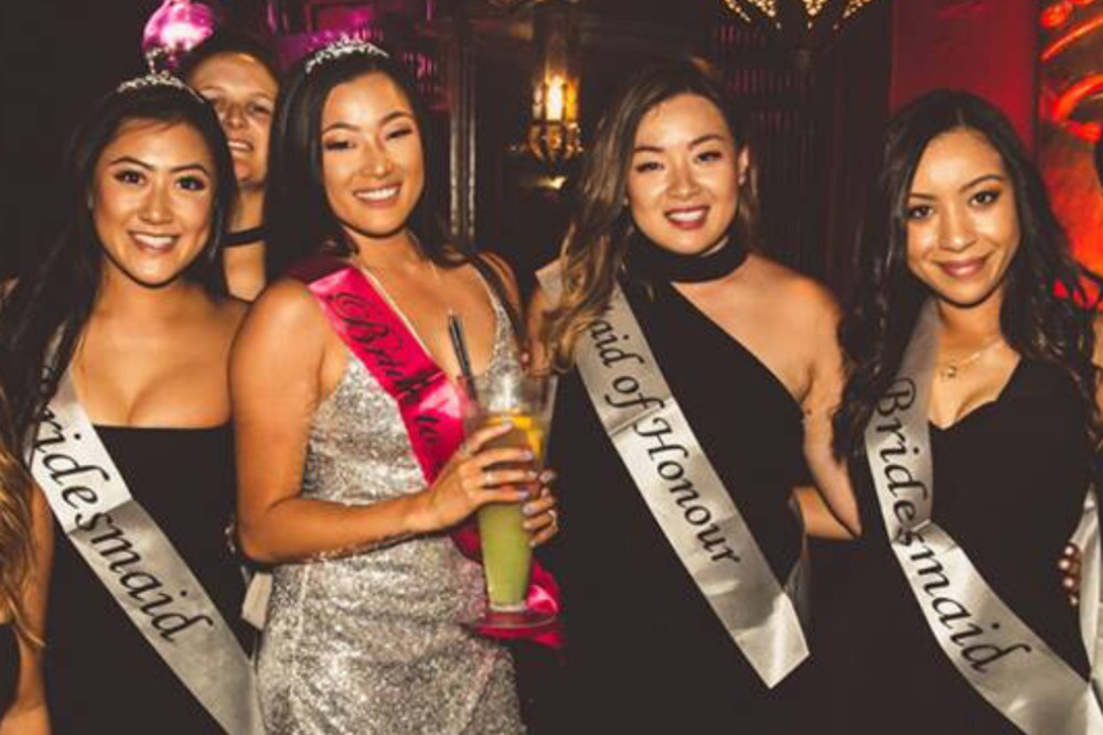 A bride to be in silver sequins with her bridesmaids in black dresses and matching satin sashes