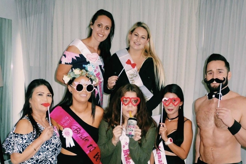 Hens in sashes holding photo props beside our topless waiter in a bow tie