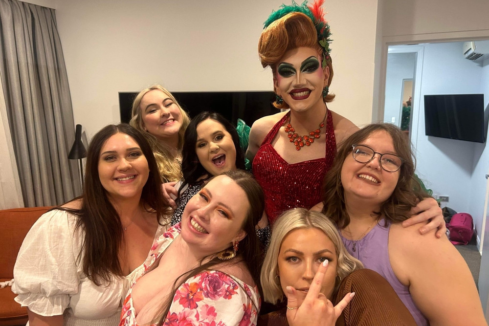 A drag queen in red sequins posing with a laughing group of hens
